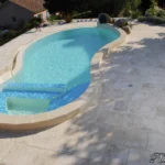 Piscine courbe avec margelles épaisses façonnées sur mesure façon pierre, région lyonnaise.