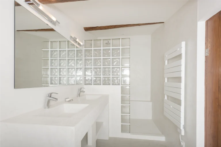 Salle de bain blanche en béton ciré Rouvière Collection avec meuble vasque et douche à l’italienne en briques de verre