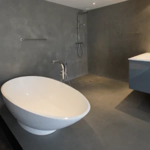 Salle de bain en béton ciré gris Rouvière Collection avec baignoire blanche originale et douche à l’italienne ouverte