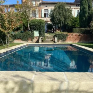 Margelle de piscine ou terrasse en pierre claire, devant une belle bâtisse pleine de charme, extérieur élégant et raffiné.