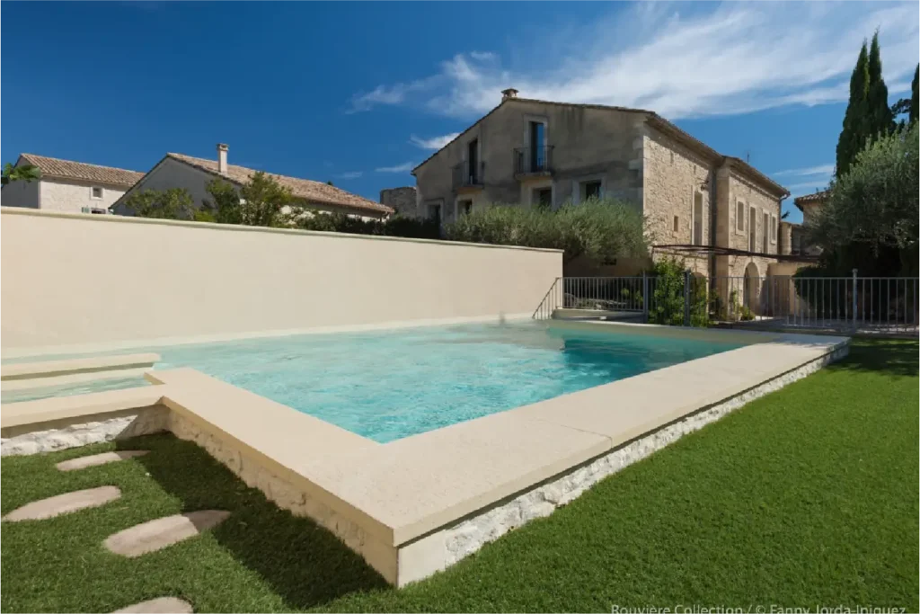 Piscine moderne avec margelles en pierre naturelle Rouvière Collection, jardin verdoyant, terrasse haut de gamme, aménagement extérieur design et matériaux nobles