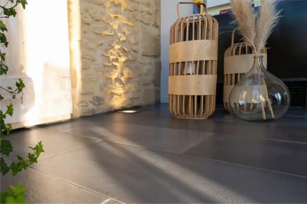 Sol intérieur en dallage bouchardé gris Rouvière Collection, pièce lumineuse moderne, décoration chaleureuse avec touches bois et beige, intérieur contemporain haut de gamme