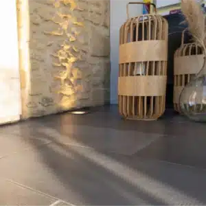 Sol intérieur en dallage bouchardé gris Rouvière Collection, pièce lumineuse moderne, décoration chaleureuse avec touches bois et beige, intérieur contemporain haut de gamme