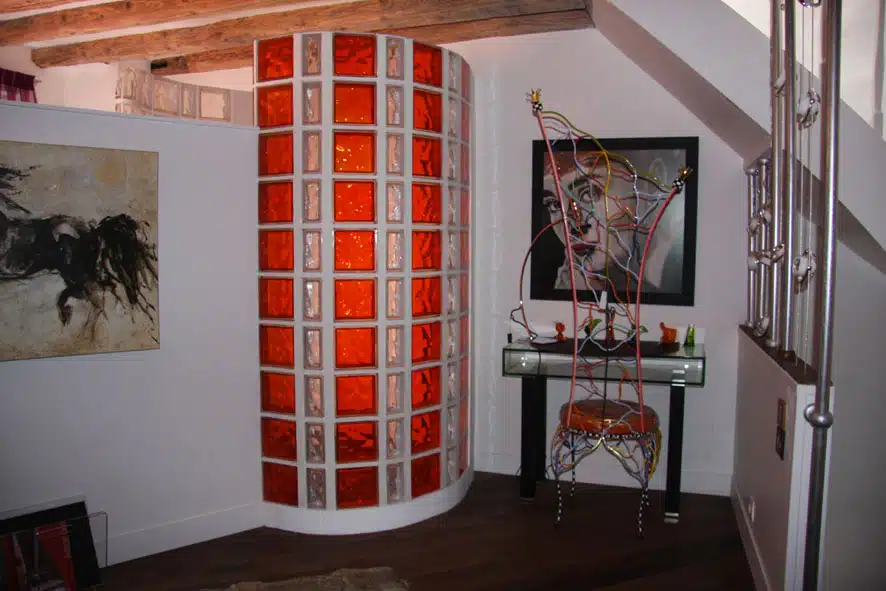 Paroi de douche courbe en briques de verre incolores et orange, lumière diffuse et ambiance chaleureuse